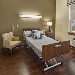 A modern hospital room with a single bed, chair, and warm lighting.