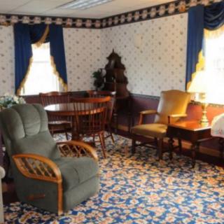 A vintage-style living room with patterned wallpaper, decorative curtains, and a mix of upholstered furniture.