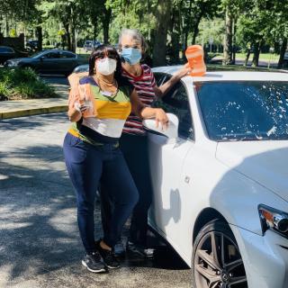 Two people wearing masks standing next to a car outdoors.