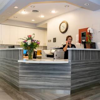 A modern reception area with a friendly staff member attending to a call, adorned with flowers and contemporary decor.