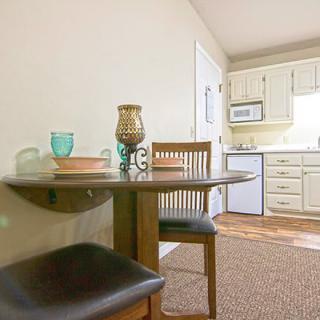 A cozy dining area with a round table and chairs adjacent to a kitchen with white cabinets.