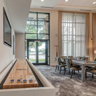A modern living room featuring a shuffleboard table and a dining area with large windows.