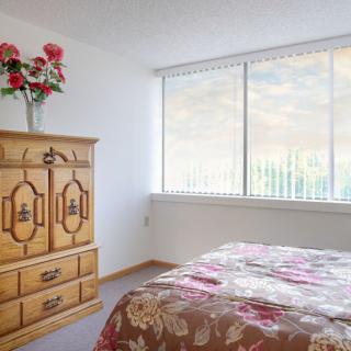 A cozy bedroom with a wooden dresser, floral bedspread, and large window.