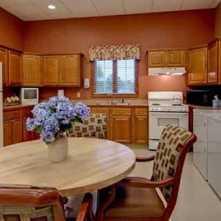 A cozy kitchen with wooden cabinets, a round dining table with chairs, and a vase of flowers on the table.