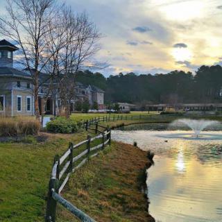 A serene view of a building beside a pond with a fountain, reflecting the colorful sunset sky.