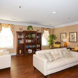 A cozy living room with a cream sofa, bookshelf, and wooden flooring, warmly lit by natural light.