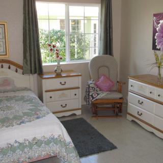 A cozy bedroom featuring a bed, dresser, and chair with natural light streaming in through the window.