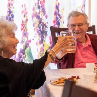 A joyful elderly couple clinking glasses while enjoying a meal together.