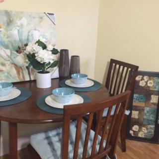 A cozy dining setup with a round wooden table, arranged with turquoise dinnerware and decorative flowers, complemented by wall art.