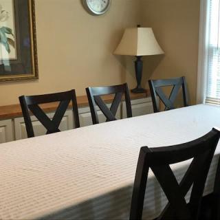 A dining room with a table, chairs, and a lamp under a wall clock.