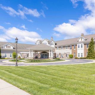 A large, elegant building with a circular driveway and neatly trimmed grass under a bright blue sky with scattered clouds.