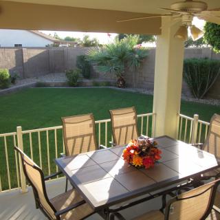 A cozy backyard patio with a table and chairs, overlooking a well-maintained lawn and garden.