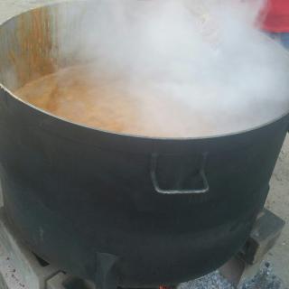 A large pot emits steam while cooking outdoors.