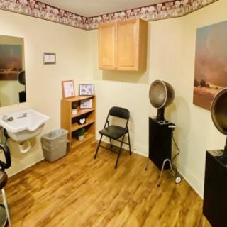 A cozy salon room with a chair, hair dryers, sink, and storage cabinets.
