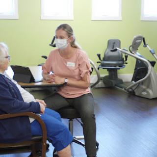 A caregiver engages with a senior client during a therapy session in a bright, indoor setting.