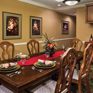 A well-decorated dining room with a wooden table set for a meal, surrounded by chairs and adorned with floral centerpiece and artwork on the walls.