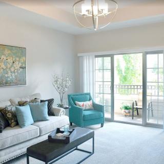A modern living room with a comfortable sofa, teal armchair, and large windows leading to a balcony.