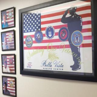 Framed military-themed artwork featuring the American flag and various service emblems on a wall.