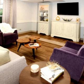 A cozy living room featuring plush armchairs, a wooden coffee table, and a television mounted above a cabinet.