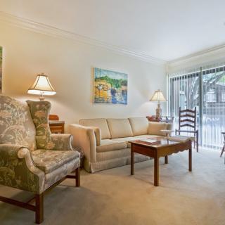 A cozy living room featuring a comfortable sofa, armchair, and coffee table, illuminated by lamps with sliding glass doors in the background.