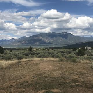A serene view of mountains beneath a partly cloudy sky, surrounded by open land and gentle greenery.