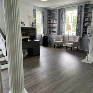 A spacious living room with hardwood floors, featuring elegant pillars, a desk area, and large windows flanked by bookshelves.