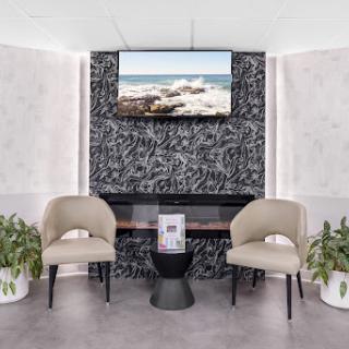 A contemporary waiting area featuring elegant chairs, a stylish side table, and a large television showcasing a serene coastal view.