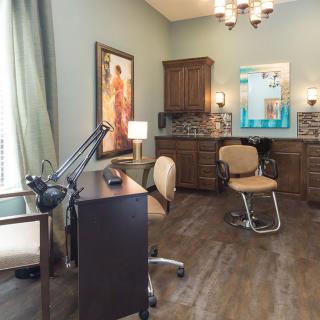 A well-organized salon room with stylish decor, featuring a styling chair, desk, and artwork.