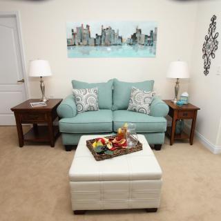 A cozy living room with a teal sofa, two lamps on side tables, and a central ottoman adorned with a decorative tray.