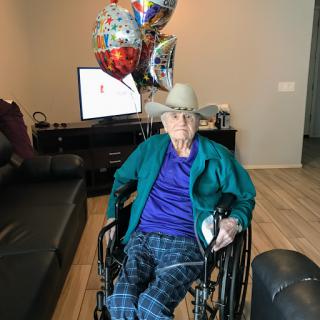 An elderly person in a wheelchair surrounded by colorful balloons, celebrating a special occasion indoors.
