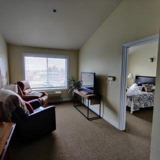 A cozy living area with an adjoining bedroom, featuring a television, armchair, and window view.