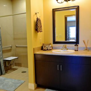 A modern bathroom with a large mirror, sink, and accessible shower space.