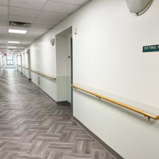 An empty hospital corridor with white walls and handrails.