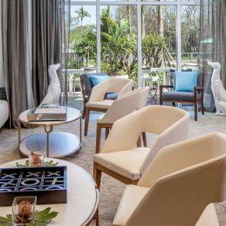 A modern living room with neutral-colored chairs, decorative elements, and large windows allowing natural light.