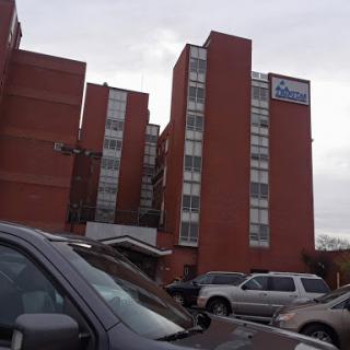A view of a brick apartment building with multiple floors, parked cars in the foreground.
