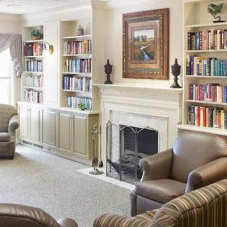 A cozy library with bookshelves, a fireplace, and comfortable armchairs.