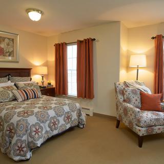 A cozy bedroom featuring a patterned bedspread, matching armchair, and warm lighting.