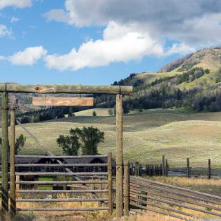A scenic view of a wooden fence with rolling hills and mountains under a partly cloudy sky.