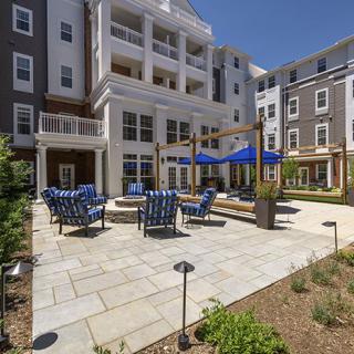 A modern apartment building with a spacious courtyard featuring outdoor seating and blue umbrellas.
