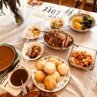 A delicious home-cooked meal spread on a table, featuring an assortment of dishes including bread rolls, gravy, vegetables, and meat.