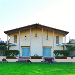 A symmetrical house with a large green lawn in front, featuring multiple doors and a sloped roof.