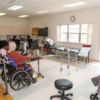A rehabilitation room equipped for physical therapy with elderly individuals in wheelchairs.
