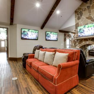 A cozy living room with a red sofa, multiple televisions mounted on the wall, and a stone fireplace.