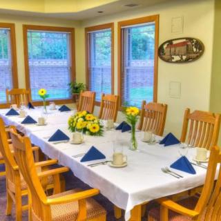 A well-set dining table with wooden chairs and floral decorations by the windows.