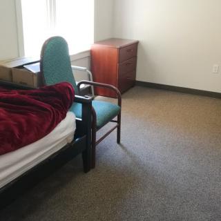 A minimalist bedroom with a bed, chair, and a window.