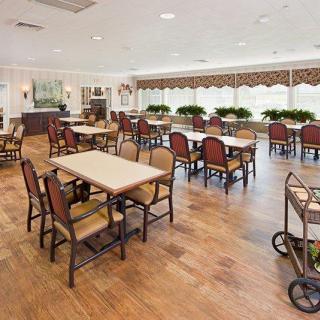A spacious dining room with neatly arranged tables and chairs, featuring a warm wooden floor and elegant decor.