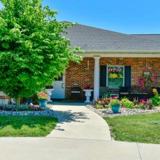 A charming brick house with a well-maintained front yard featuring colorful plants and a tree.