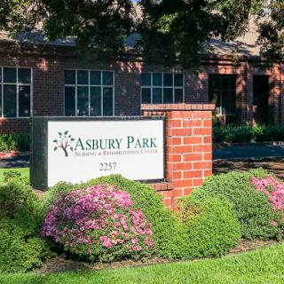 A welcoming entrance sign for Ashbury Park, surrounded by lush greenery and colorful flowers.