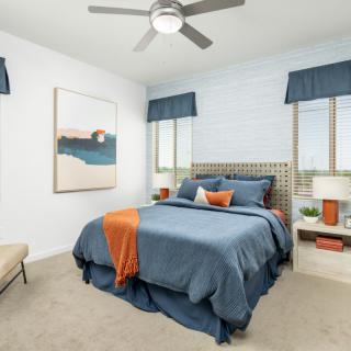 A modern bedroom with blue bedding and orange accents, featuring large windows and stylish decor.