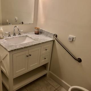 A bathroom with a sink and vanity, featuring a marble countertop and a grab bar.